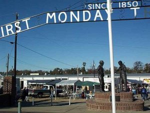 The sign says First Monday - Since 1850.  In the back are bronze statues of two men - perhaps a woodsman and a rancher - met to trade, sometime in the past.