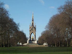 A gothic tower covers the statue erected by Queen Victoria in memory of Prince Albert; the view shows the tower against a blue sky, with a long row of trees on each side.