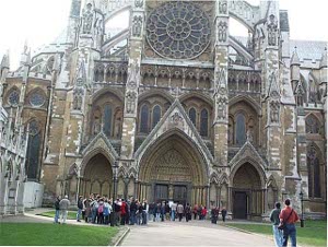 Looking like a mottled brown and white building, Westminster Abbey shows flying buttresses and crowds waiting to enter