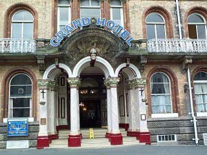 Built of tan stone, with brown stone surrounding the windows, white pillars connected by arches in front, with bright carmine pediments and a blue neon sign, the Grand Hotel is clearly a Victorian edifice of some standing, if not beauty