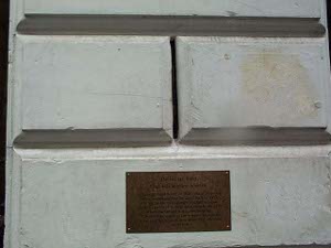 It's quite easy to miss that this is a window -- the narrow slit between two blocks of stone might be half an inch wide, and eight inches tall, approximately.  Only the brass plaque below draws the visitor's attention