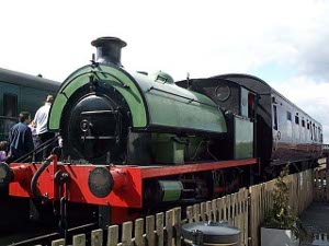 The green steam locomotive has a very heavy iron frame with pusher bars; it is displayed outside