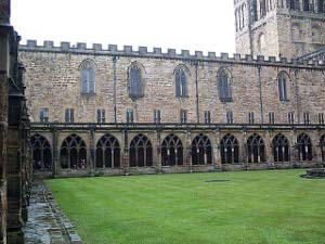Surrounding the grassy inner square of the cloisters is a brick arched gallery; one tower of the cathedral rises over one corner.