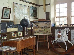 On view are a globe, teacher's desk, rocking horse, maps, models of animals, etc.