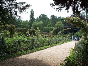 A tan gravel path leads from Monet's house to the garden at Giverny, flanked with greenery and flowers