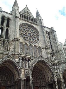 The large rose window on the wall sits above the three massive parallel doors, the whole structure adorned with arches, windows, towers and carvings