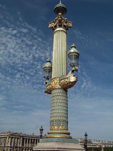 The enormous street lamp is an ornate turquoise and gold column, with two arms half way up holding lamps, and a crowning decoration on top