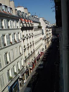 A long line of 5-story apartment buildings stretches down this typical Parisian street.  The ground floor is taken up with stores and businesses.