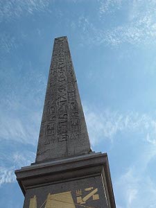 The Egyption obelisk is mounted on a column along the Champs Elysees.  Writing and diagrams on the black and gold base explains the obelisk.