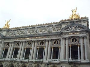 The front of the opera has elaborate friezes, balconies, and gilt decorations, with huge gilt sculptures on the roof