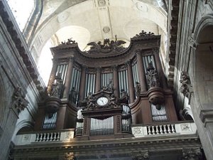 The Organ pipes are enclosed in an elaborately carved dark wood frame, which sits atop a marble balcony under the romanesque cathedral ceiling