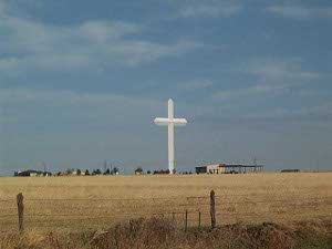 Seen from a distance, the cross stands tall and white above the beige grasses of the Texas prairie