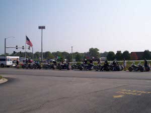 By the side of the road the motorcycles line up, two by two.  At the front of the line is an RV and a large American flag.  They are all going to the Harley Davidson celebration in Milwaukee.
