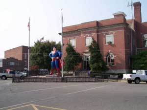 In the square in front of the small two-story brick city hall of Metropolis, Illinois, stands a blue and red statue of Superman, flanked by flagpoles.