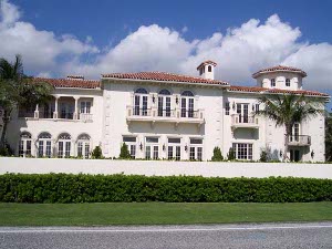 The two story white mansion has a red tile roof and imposing architecture facing the ocean