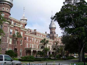 The red brick building has cream window trim, a large porch, and startling silver-colored domes on top of its towers