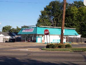 This white building with a turquoise blue roof has a big banner sign reading 'DAIQUIRIS' in red letters on white, across the front roof.  Another sign points to the drive through window