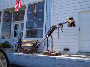 Made of junk metal and sitting on the porch of a white clapboard building, Porchosaurus Wrecks vaguely resembles Tyrannosaurus Rex