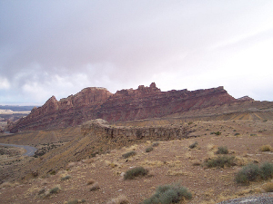 The massive stone reef, with long slanting lines of geological significance, arises out of a sandy tan valley in Utah