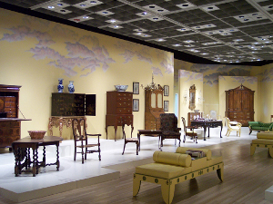 The well-lit furniture gallery has pieces displayed on a white raised platform.  Included are living room, dining room and bedroom furniture