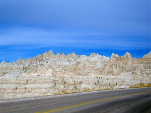 Against a blue sky with thin white clouds, the jagged peaks and tan and white stripes of the badlands make a beautiful picture