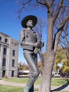 The bronze statue, next to a tree in front of the courthouse, shows Jones, a tall, slender man with a rope draped around his shoulders, a wide-brimmed hat, holding his work gloves, and wearing boots.