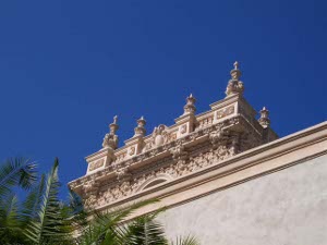 Detail showing the light tan roof decorations against an azure blue sky, with green palm fronds in the foreground