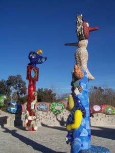 Two tall ceramic totem poles in bright colors have beaks and bills, arms and snakes, and of course bright rainbow colors
