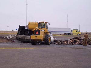 A yellow Highway Department front-loader scoops burnt debris off the roadway and into a waiting dump truck at the scene of a spectacular accident