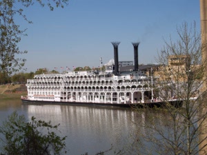 A large four-deck white steamboat with tall black smokestacks sits on the Mississippi