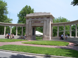 A semicircular pillared and pedimented wall surrounds a massive square arch in Tappan Square, surrounded by greenery.  Students and alumni sit on the wall.