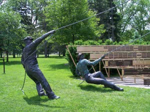 Two bronze men lean over backward, apparently tugging on bronze ropes to raise the tent for the Shakespeare Festival