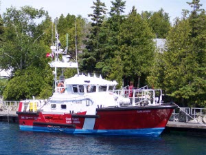 The superstructure is white, the upper hull red on top and light blue below, with an iron rail all around the deck on this Coast Guard workboat, about 35 feet in length