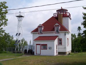 The two story lighthouse is painted white with a red roof; the light tower rises above the top of the roof, and a solar power tower has been erected nearby