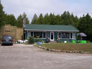 A small green frame building with a gravel driveway for a parking lot, and an outside table with an umbrella, the Stone Orchid is the best restaurant near Tobermory