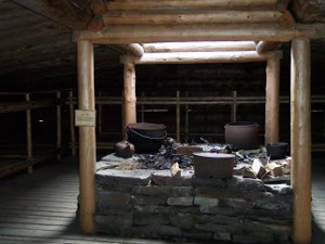 The hearth sits in the center of the square bunkhouse lined with two tiers of bunks; aside from the stone hearth, all is built of bare logs.