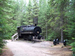 A black steam locomotive located in a sandy clearing at the Logging museum