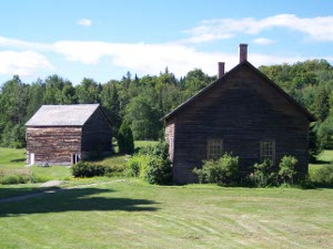 House and barn in dark weathered wood, surrounded by mown fields