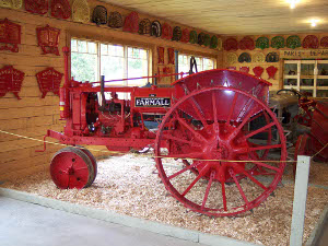 The bright red farmall tire has big metal spiked wheels.  It is on display inside a garage filled with tractor parts