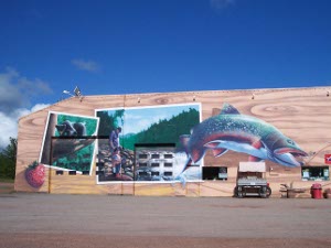 A mural in Dorion depicts photographs of fishermen and a huge trout against a background of an oversized piece of plywood