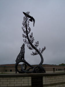 A black metal sculpture showing a wolf and a pine tree with an eagle on top