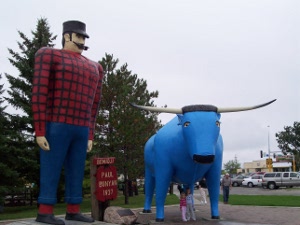 The statues of Paul Bunyan in a red and black lumberjack shirt, black hat, blue jeans, red sox, black shoes, smoking a pipe, with a long straight black mustache, and his longhorn ox Babe the Blue Ox in a brilliant shade of blue brightens Bemidji, Minnesota