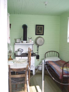 A miner's one-room cabin, with a bed, stove, table, and wash basin hanging on the wall