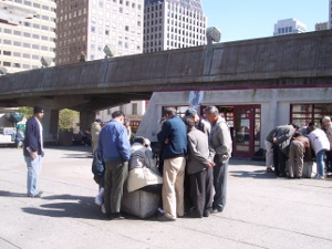 a crowd of ten men are clustered around a game table where two men are playing Chinese Checkers