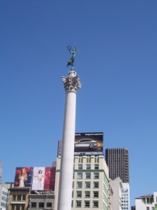 The bronze statue of victory holding a laurel wreath stands on top of a very high pedestal in Union Square