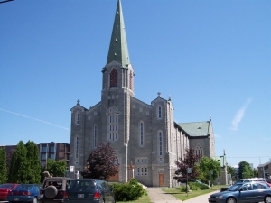 A solid Quebecois church, of grey stone with tall narrow windows and a green roof, Montmagny