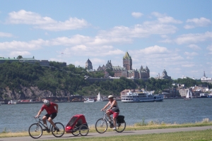 Two bicyclists along the path with the St. Lawrence, a cruise boat, and the famous Chateau Frontenac in the distance