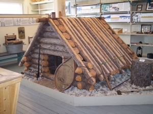 The Hudson's Bay Company museum features a reproduction of a trapper's tilt, five feet high, made of logs, with a tiny crawl hole, snowshoes resting outside against the building.
