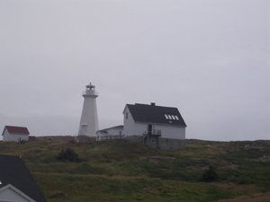 All white, the Cape Spear lighthouse is flanked by service buildings on top of a windblown treeless hill
