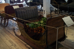 An old two-person horse-drawn sleigh with leather seats and a colorful blanket, in the carriage house at the Shelburn Museum.
